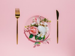 Table setting with pink plate full of flowers and egg with golden spoon and knife on pink background. Creative fine dining of food concept. Contemporary healthy breakfast arrangement. Flat lay.