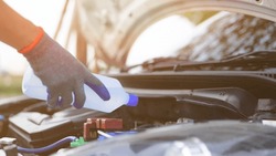Man holding distilled or deionized water to refill car battery. Car inspection and maintenance concept.