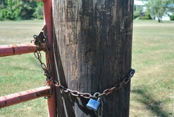 Chain and Lock on Rustic Wooden Post and Rusty Metal Gate 