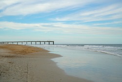 People walking along St Augustine Beach with pier in the background.