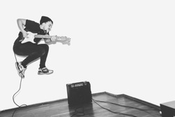 Awesome crazy fashion young rock guitar player jumps with passion in studio. Black and white toned. White background.
