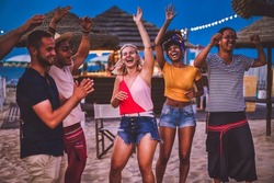 Group of happy multiracial friends dancing at sunset beach party in summer vacation - Young millennials people having fun at weekend in the outdoor  club - Youth lifestyle and nightlife concept