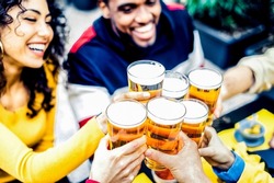 Group of friends toasting a glass of beer in courtyard of the brewery pub - Happy people cheering lager pint at the restaurant bar - Friendship, smiles and youth lifestyle concept - Focus on glasses