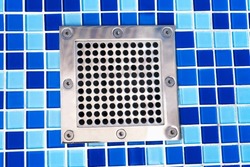 Close-up of water drain filter at the bottom of the swimming pool. Empty blue swimming pool with steel drain grid.
