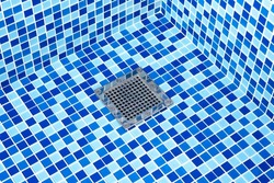 Water drain filter at the bottom of the swimming pool. Empty blue swimming pool with steel drain grid.