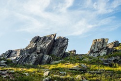 Sunny highland scenery with sharpened stones of unusual shape. Awesome scenic mountain landscape with big cracked pointed stones closeup among grass under blue sky in sunlight. Sharp rocks with cracks