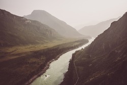 Vintage misty mountain landscape with wide mountain river in sepia tones. Gloomy scenery with confluence of two mountain river in mist. Atmospheric view to confluence of great rivers in faded colors.
