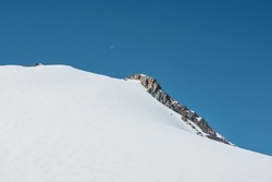 Minimalist view to snow mountain top with sharp rocks in sunlight. Snow-white mountain under blue sky in sunny day. White and blue snowy minimal landscape. Simple minimalism with snow-covered mountain