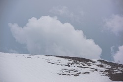 Atmospheric alpine landscape with high snow mountain wall under rainy clouds in gray sky. Dramatic overcast scenery with large snowy mountain top under gray cloudy sky. Gloomy weather at high altitude