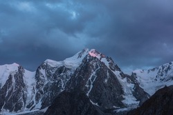 Atmospheric landscape with sunset pink reflection on huge snowy mountain top in dramatic sky. Hanging glacier and cornice on giant snow mountains in dusk. High snow-covered mountain range in twilight.