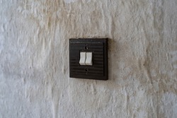 Filthy old square light switch on a wall. Retro toggle switch in an East German apartment. Interior design of the past in a bad condition. Dirt stains and dust on the wallpaper.