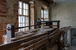 Old machine in an abandoned factory. Dirt and dust lying around in a damaged room. The walls are eroded and bricks come through the plaster. Vintage machinery in an old building.