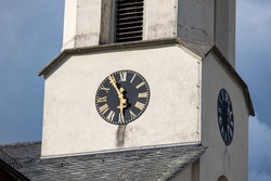 Close up white church tower with white clock. Ancient clock with old black clock-face and golden watch hand. Sunny day with blue sky and few clouds.