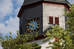 Close up church tower with clock. Ancient clock with blue and golden shiny clock-face. Sunny day with blue sky and few clouds.