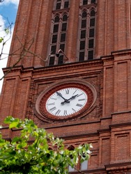 Church clock. Red brick church tower with ancient black and white clock-face. Sunny day with blue sky and few clouds.