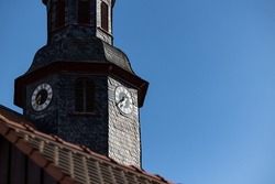 Church clock. Close up church tower with roff shingles. Ancient clock and old white, black and golden clock-face. Sunny day with blue sky and few clouds.
