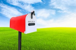 Red post mailbox with blured outdoor green lawn grass and blue sky on background.