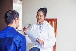 Young female Indian doctor consulting a patient while holding medical reports and prescription medicines in her hands