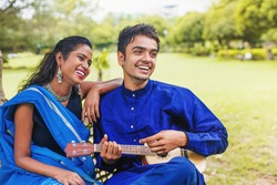 Beautiful indian couple in ethnic clothes playing guitar in a park and singing