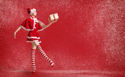 Dancing ballerina girl in pointe shoes with gift in her hands dressed as Santa Claus on red background.