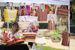 Crafts fair booth filled with woven bags and purses in bright colors outside on a sunny morning
