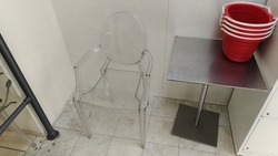 In the store lobby, there is a clear plastic chair on the tile floor, a metal table with plastic baskets with handles for customers
