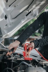 Close-up of auto mechanic charging car battery with electric rail jumper cables