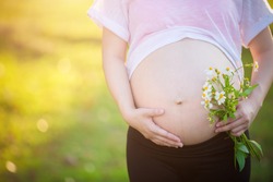 Close up of pregnant woman are relaxing in the garden at house. pregnant woman holding her belly and flower in the garden