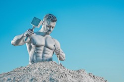 Legendary courage Atlas creating his perfect body from rock. Close up of strong well biuld man with hammer in right hand and chisel in left looking down. Isolated on blue studio background.