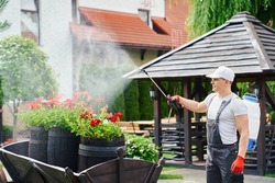 Professional male gardener in uniform, safety glasses and gloves using aerosol chemical protection from pests while working at garden. Concept of people, plants and seasonal work. 