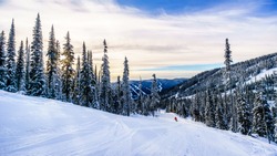 Skier going down the ski slopes surrounding the alpine village of Sun Peaks in the Shuswap Highlands of central British Columbia, Canada on a late afternoon 