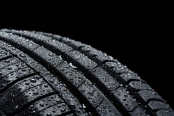 Car tire covered with water drops on black background