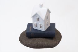 A small, white ceramic house sitting on a vintage holy bible on a big rock. A simple, abstract representation about building your life on God. Horizontal with copy space.