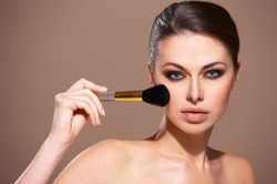 Portrait of beautiful woman applying cosmetic isolated on beige
