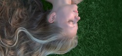 a close-up portrait of a beautiful young girl with long blonde hair, eyes closed, lying upside down on the green grass