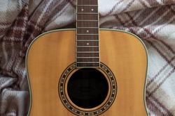light wood guitar without strings with black hole and brown patterns on a woolly brown checkered plaid