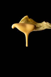 Closeup photo of a nacho with liquid cheese dripping from it on a black background