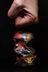 Closeup photo of an aluminum can being smashed by a male hand over a black background. Concept photo to represent recycling, waste, metal, etc.