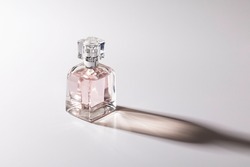 Pink glass perfume bottle with delicate colors and long shadows on the white background. No name bottle for representation.