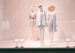 Three mannequins with summer clothes stand in a shop window in a shopping center. Summer clothes, white mannequins.