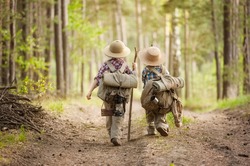 Two boys go hiking with backpacks on a forest road bright sunny day