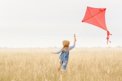 Little girl runs outdoors. Cheerful and happy child plays and launches a kite in the field against the blue sky. Kid dreams of flying and aviation.