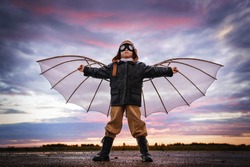 Boy with wings at sunset imagines himself a pilot and dreams of flying