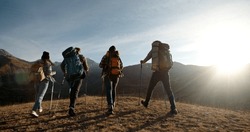 Group of four young people having a hiking tour, going for trekking adventure together, reaching top of mountain and cheering - friendship, achievement concept 