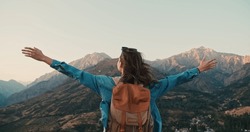 Overjoyed happy woman enjoying beautiful nature mountains around her.Young girl standing on top of mountain and victoriously raising hands up, looking far away. concept of happiness emotion