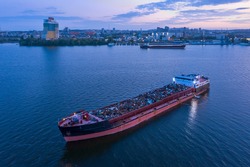 A ship loaded with scrap metal is anchored in the water area of the Dnieper River against the background of the evening city of Dnipropetrovsk