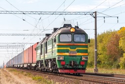 A powerful green diesel locomotive 2M62 pulls a freight train along the tracks of a railway station. Autumn photo.