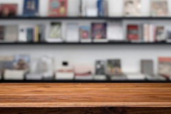 Empty wooden table platform and blur background of library or book store setting with books and reading material. Can be used for montage or display your products.