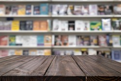 Empty wooden table platform and blurred background of library or book store setting with books and reading material. Can be used for montage or display your products.