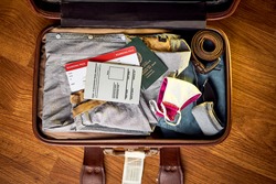 An image of a packed suit case on a wooden floor of a South African man who has received his covid vaccine and has a certified travel certificate along with his passport and flight boarding pass